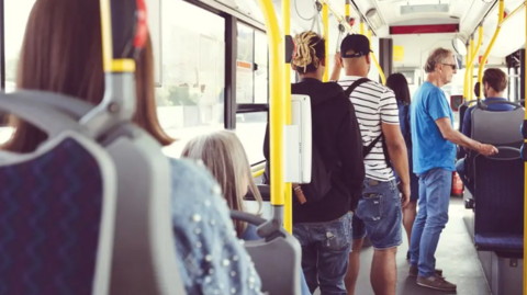 People stand and sit on a bus.