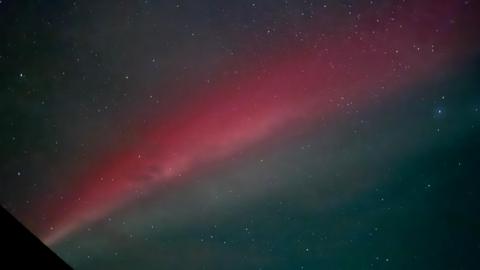 The night sky with stars filling the sky and a large streak of red representing a Strong Thermal Emission Velocity Enhancement, also known as Steve