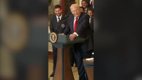 Lionel Messi (left) stands next Donald Trump (right) who is behind a podium. Both are suited