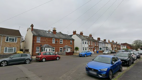 A general view of a residential street with a mix of semi and detatched houses and cars parked on the road in the foreground