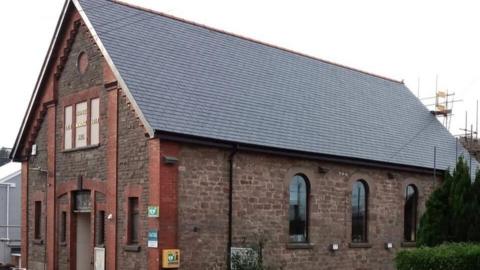 An old red brick building is seen with a new slate roof. 