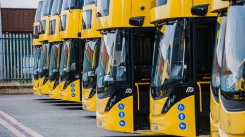 A row of yellow Bee Newor, double-decker buses, lined up at a depot. 