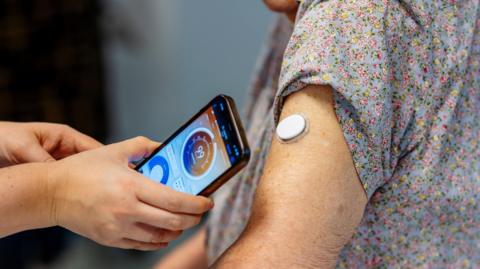 A digital blood glucose monitor on a woman's arm