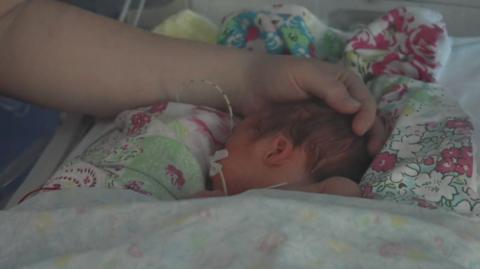 A newborn baby sleeps peacefully, with a parent's hand stroking her head 