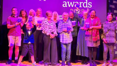 All of the winners stood in front of a purple make a difference awards board holding their awards