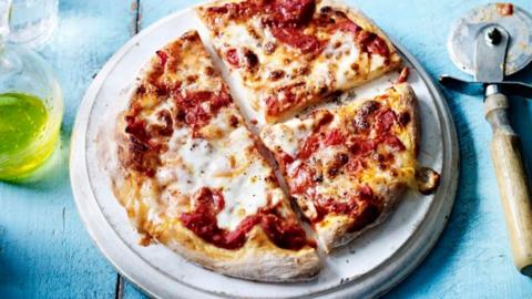 A homemade pizza on a white plate with a blue background