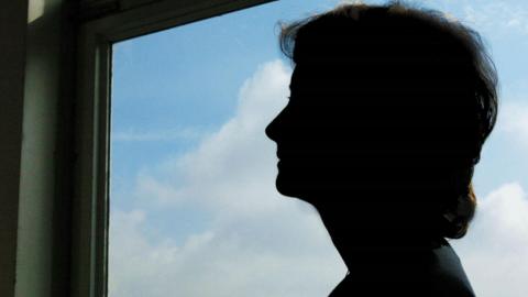 Silhouette of a woman's head and shoulders against a window showing blue skies.