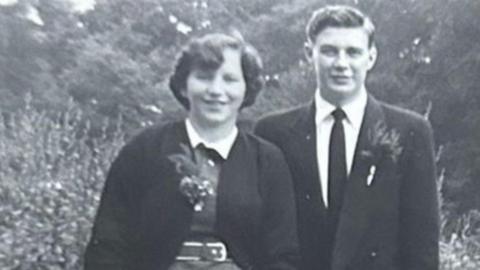 Pat and David Johnson dressed smartly looking to camera on their wedding day in 1955 in a black and white photo