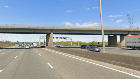 The M1 motorway with a bridge running above it. Vehicles travel on either side of the motorway on a sunny day.