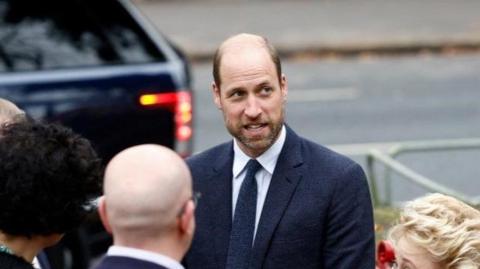 Prince William is wearing a dark navy suit and tie. 