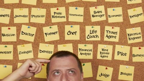 Man thinking with a pinboard in the background, sticky notes with job titles one it