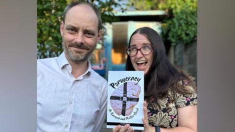 A man and a woman pose together - the man, wearing a white shirt, is smiling and has thinning grey hair and a grey beard, while the woman has long brown hair, is wearing glasses and a black top with a pink and beige pattern on, and is looking away as she holds her mouth open. The book's cover features a brain wearing a black leather harness and the title "Pornocracy"