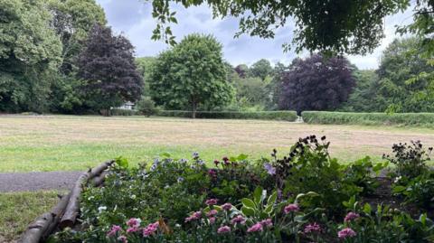 A bed of pink flowers with a path and Elvet Bowling Green's neatly-cut grassland behind.
