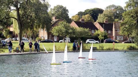 People on edge of lake with model yachts on the water