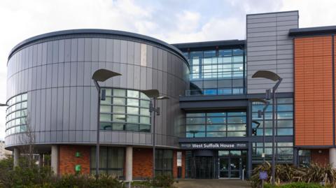 A view of a council building with large windows above its entrance and grey and red panels that cover its exterior,