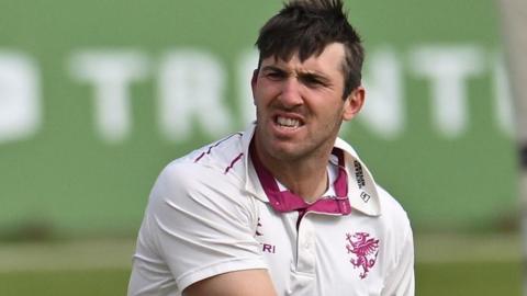 Craig Overton wearing a white Somerset shirt grits teeth