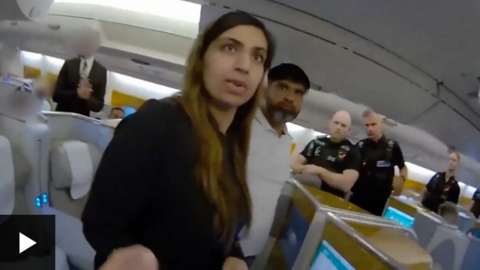 A still image of two people being detained on an plane