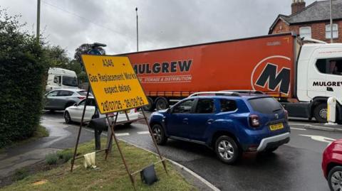 A traffic-clogged road with a yellow sign warning of roadworks and delays 