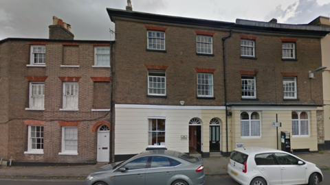 A Google Maps picture of the town council's headquarters, a 19th Century, three-storey, mid-terrace building with two cars parked on the road outside. 