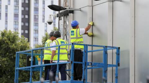 Workers remove cladding from a building