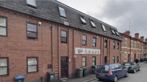 The Annex, Coventry, is a long red brick building with a blue car parked outside and a green mini cooper car also parked outside.
