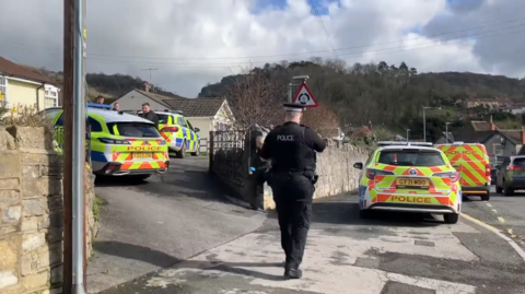 The rear of a police officer and four police cars surrounding a property