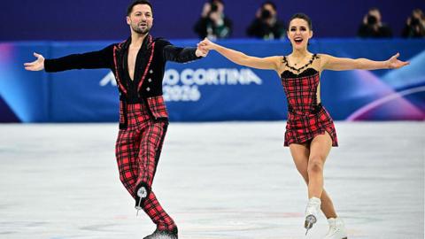 lilah fear and lewis gibson holding hands and skating together on ice.