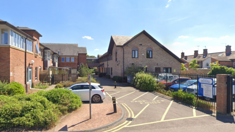 The former Pershore police station pictured from a car park. The building is fenced off by a metal gate and is made up of cobbled bricks. The roof has a triangle shape to it and the building is comprised of two floors. 