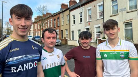 Four young men in running kit standing in front of a row of terraced housing.  