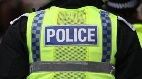 Police officer wearing hi-vis uniform with back to camera
