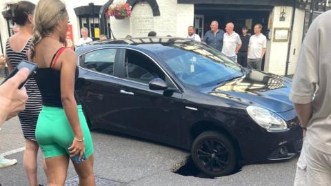 Car with wheel in sinkhole in Witham