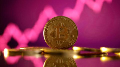 A photo showing a gold bitcoin with a pink background