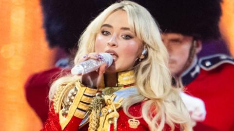 Sabrina Carpenter performs live during The BRIT Awards 2025 at The O2 Arena on March 01, 2025 in London, England. She is dressed in red and her dancers are wearing bearskin hats 