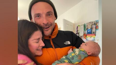 A mum and dad holding a baby.