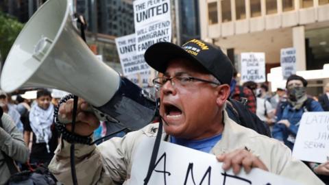 A man screams into a bullhorn wearing a US Navy hat in Chicago.