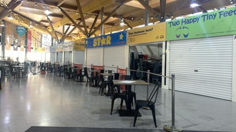 The interior of Moor Market, an open communal space with retail units and tables and chairs.