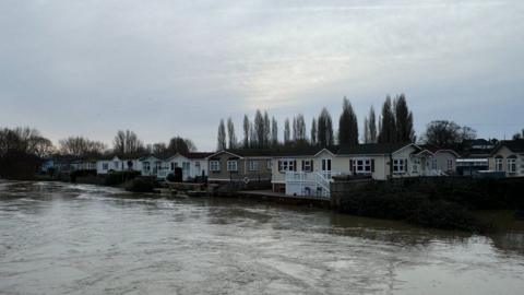 The River Stour at a very high level with a row of mobile homes at the far side of the river.