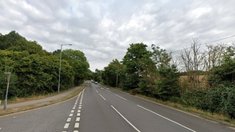 A junction entrance on the left leading into Gallows Hill, a single lane carriage lined by bushes.