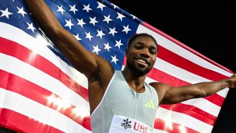 Noah Lyles celebrating with an American flag after winning a race