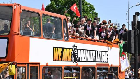 Hull City players wave to fans as the ride on the top deck of an open-top red bus