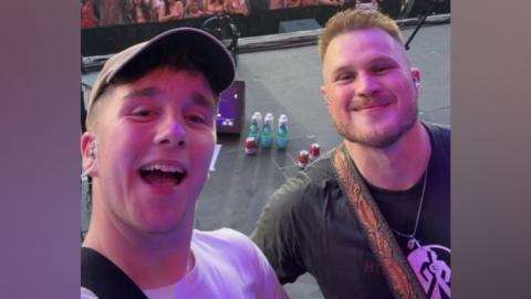 The image is a selfie of Paul with Zach Bryan. They are standing on a stage.