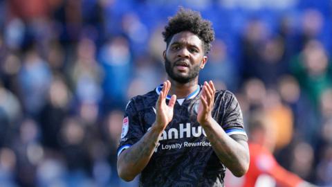 Bristol Rovers forward Ellis Harrison wearing a black away shirt and applauding fans at the end of an EFL match