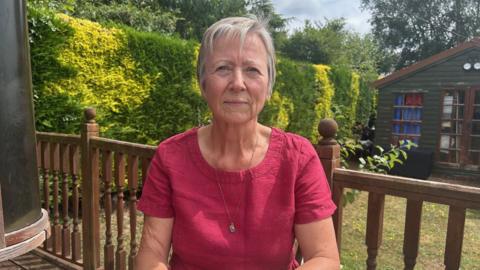 A woman in a dark pink top and grey hair sitting at a garden table