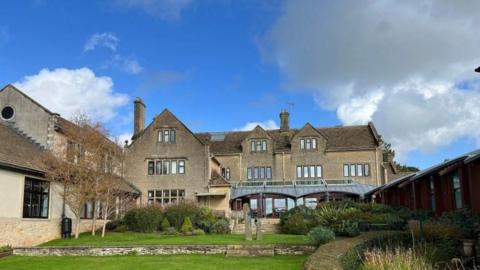 Dorothy House's base in Winsley, as seen from the back showing the garden. It is a large three-storey house with extensions and a glass conservatory.