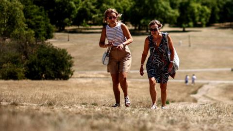 People make their way along a path through the dry, sun-scorched grass of Primrose Hill, backdropped by the skyline of central London, on July 27, 2026.