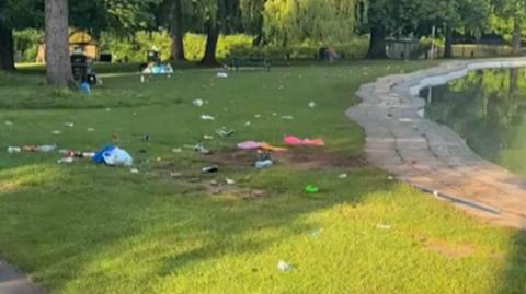 A park scene with a pool on the right and trees at the background. The grass is covered with litter.