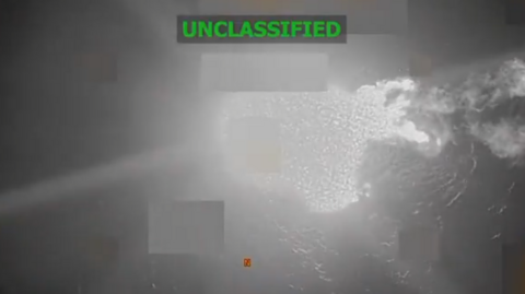 What appears to be a black and white image of the sea as seen from above. A few areas are blurred, including the section where the boat is. A large white area which appears to be the flames of an explosion are in the centre of the image. The word "unclassified" is captioned on the image. 