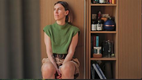 Milda Mitkutė - Founder of Vinted - sits in a room next to wooden shelves. She is wearing a green top.
