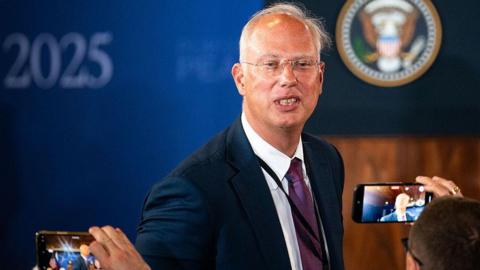 Kirill Dmitriev in a blue jacket poses for photographers in Alaska with whispy silver hair and transparent glasses