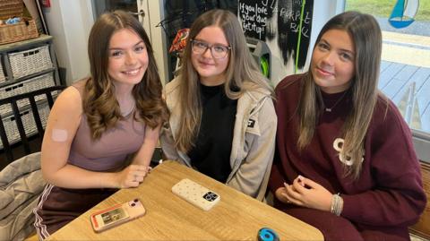 Three female students in a cafe with their phones on a table in front of them